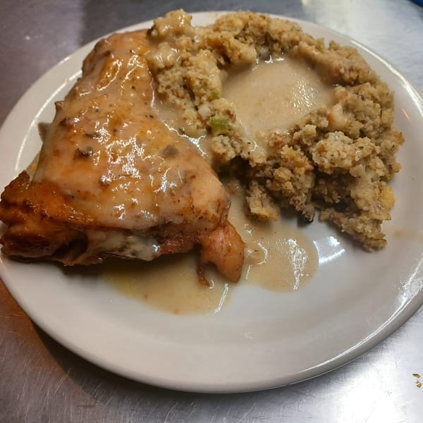 A plate of Jess Soul Food's baked chicken with gravy and a side of cornbread dressing.