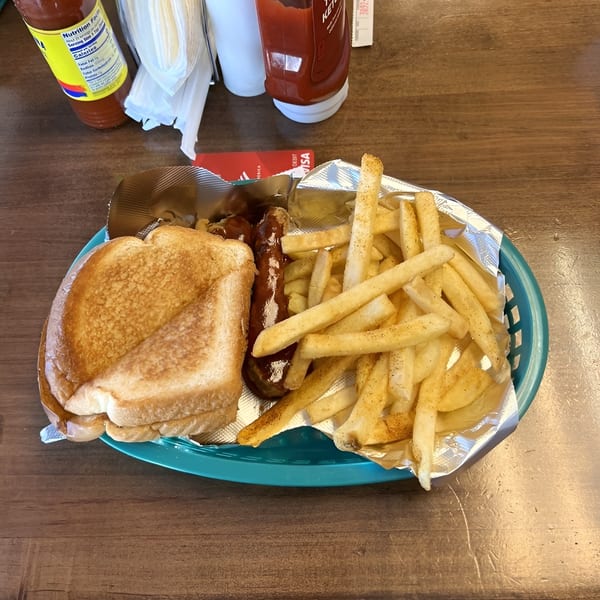 A basket of soul food with a grilled cheese sandwich, hot dog, and seasoned french fries.