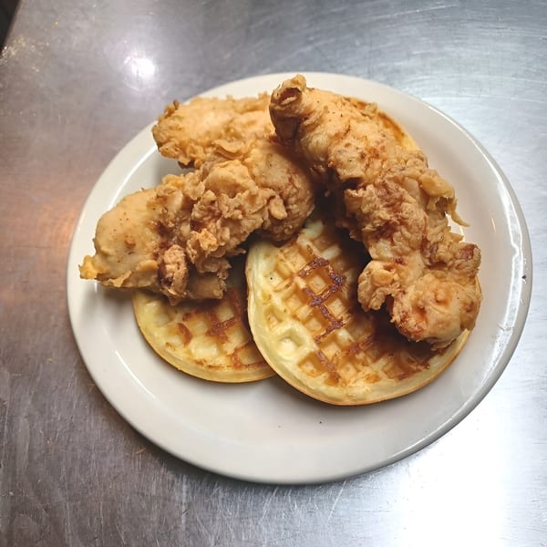 Crispy fried chicken tenders served on two golden waffles on a white plate.
