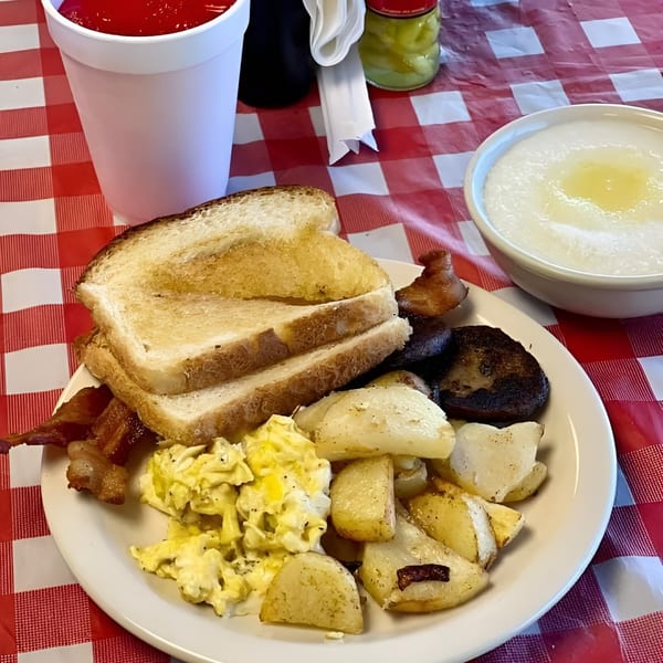 A soul food breakfast plate with scrambled eggs, home fries, bacon, sausage, toast, and grits.